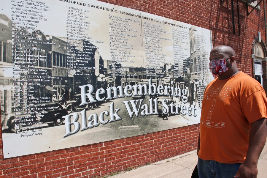 FILE - In this June 15, 2020 file photo, Freeman Culver stands in front of a mural listing the names of businesses destroyed during the 1921 Tulsa Race Massacre in Tulsa, Okla. Attorneys for victims and their descendants affected by the 1921 massacre filed a lawsuit in state court on Tuesday, Sept. 1, 2020, against the City of Tulsa and other defendants seeking reparations for the destruction of the city's once thriving Black district. (AP Photo/Sue Ogrocki File)